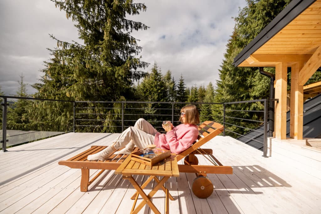 Woman lying on lounge bed while resting on spacious white terrace of house in mountains. Recreation and escaping to nature concept
